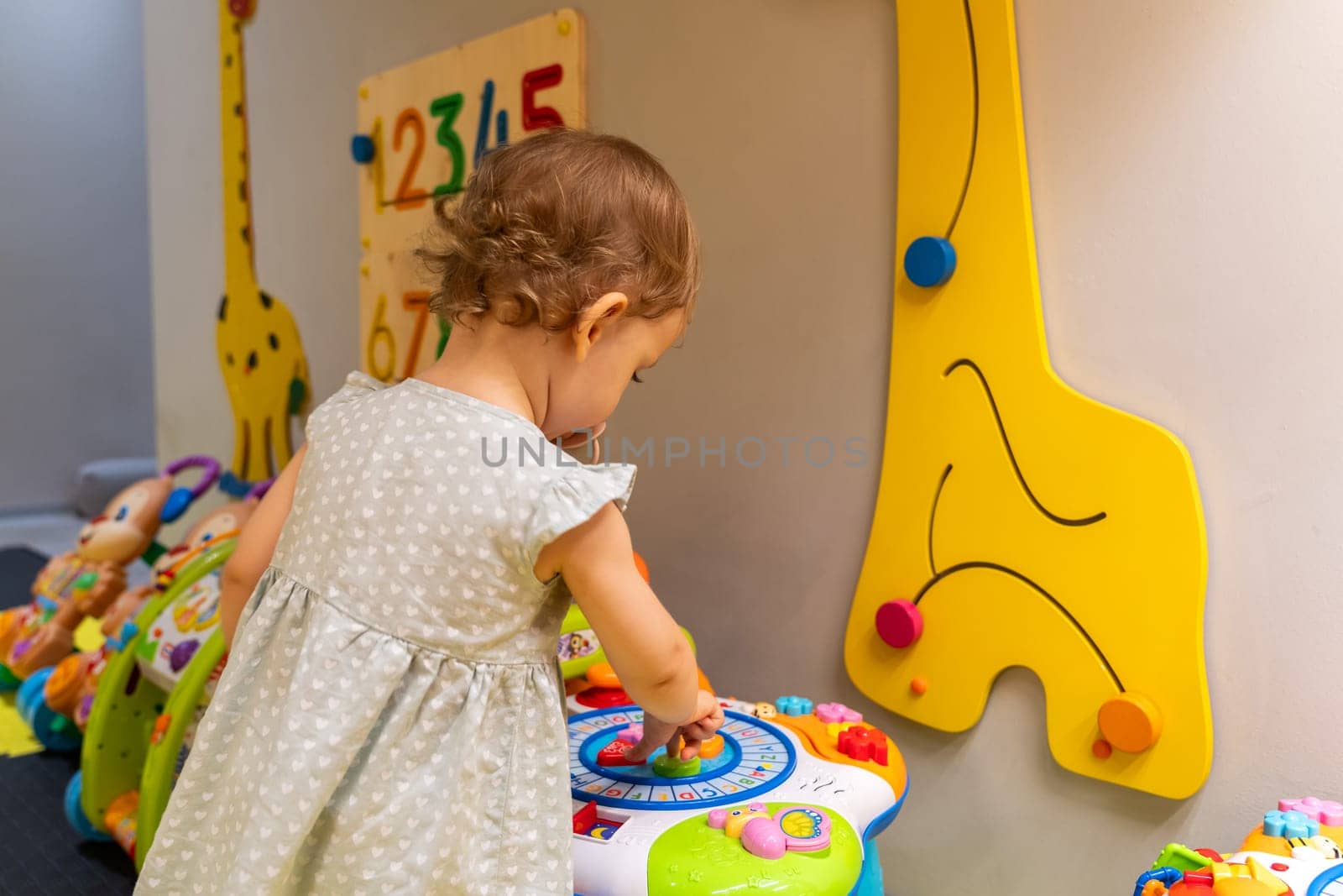 Toddler exploring a colorful activity table in an engaging playroom, discovering shapes and sounds. Concept of early learning and fostering creativity through interactive play