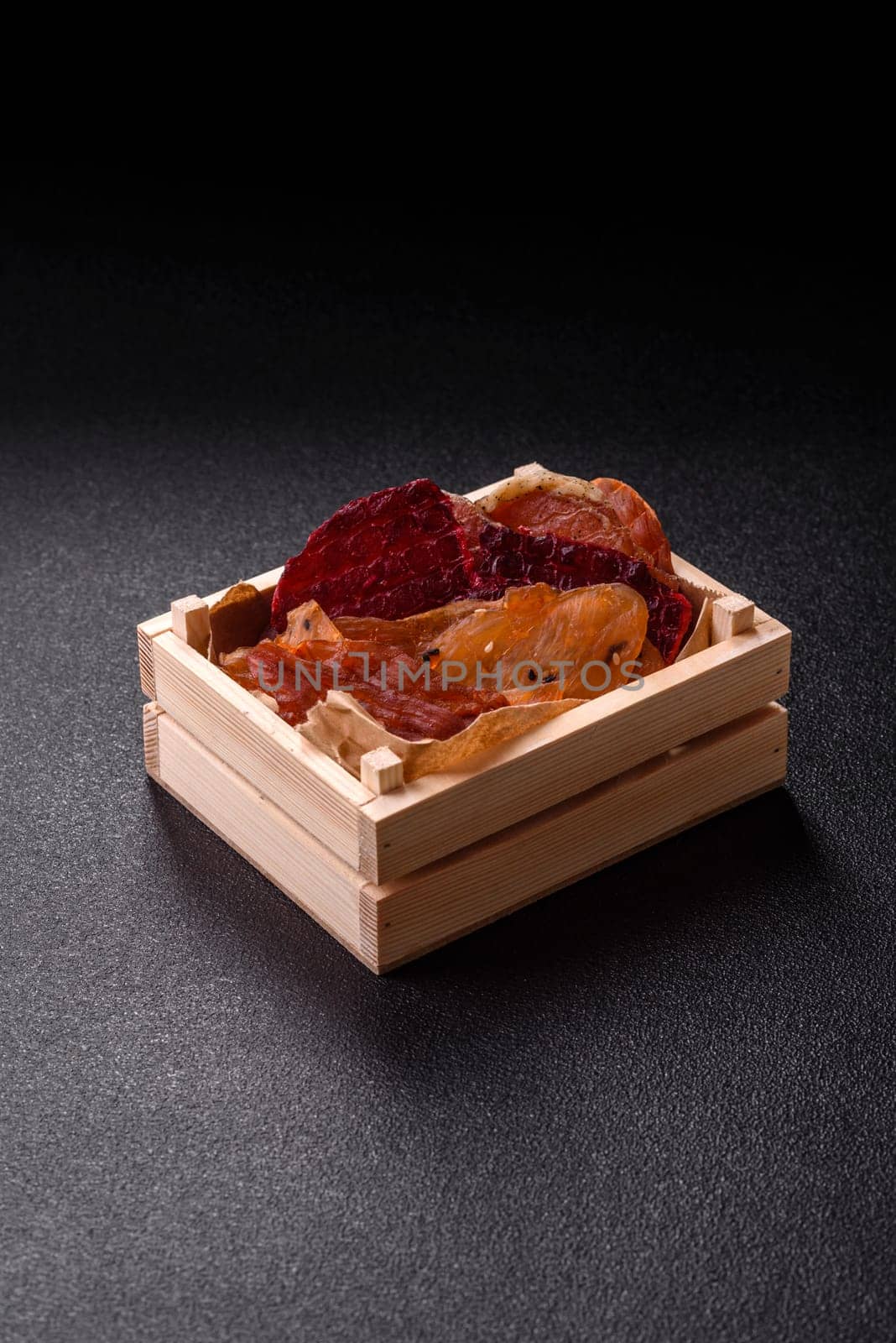 Jerky, dried meat in the form of slices with salt, spices and herbs on a dark concrete background