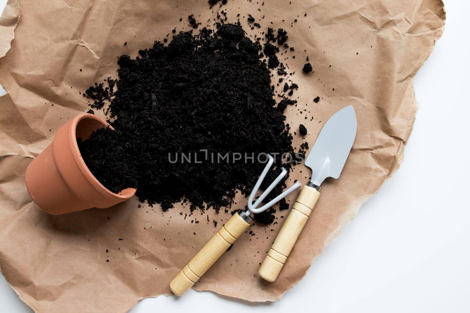 Garden tools with soil and pot on brown paper background.