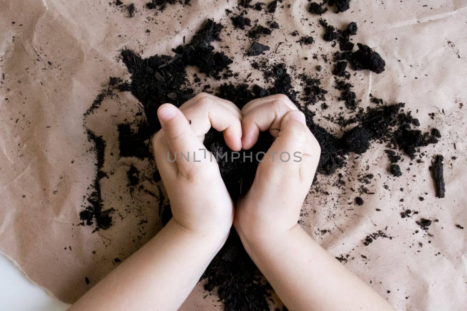 Childs hands forming heart shape in soil on brown paper background.