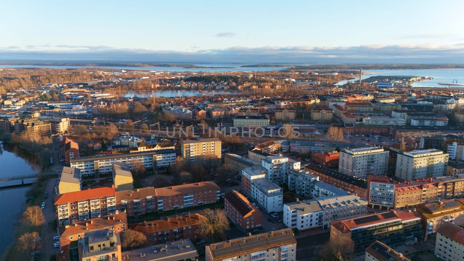 A scenic aerial view of Karlstad, Sweden, with warm sunset light illuminating the cityscape, residential buildings, and waterfront, creating a peaceful and picturesque atmosphere.