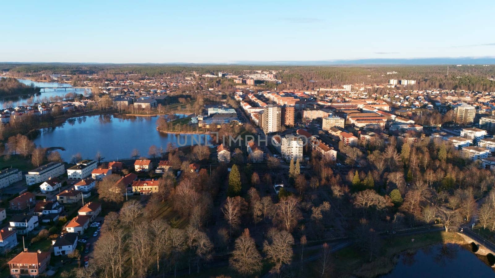 A scenic aerial view of Karlstad, Sweden, featuring lakes, lush parks, and residential areas bathed in golden sunset light, blending nature and urban charm in a peaceful Nordic setting.
