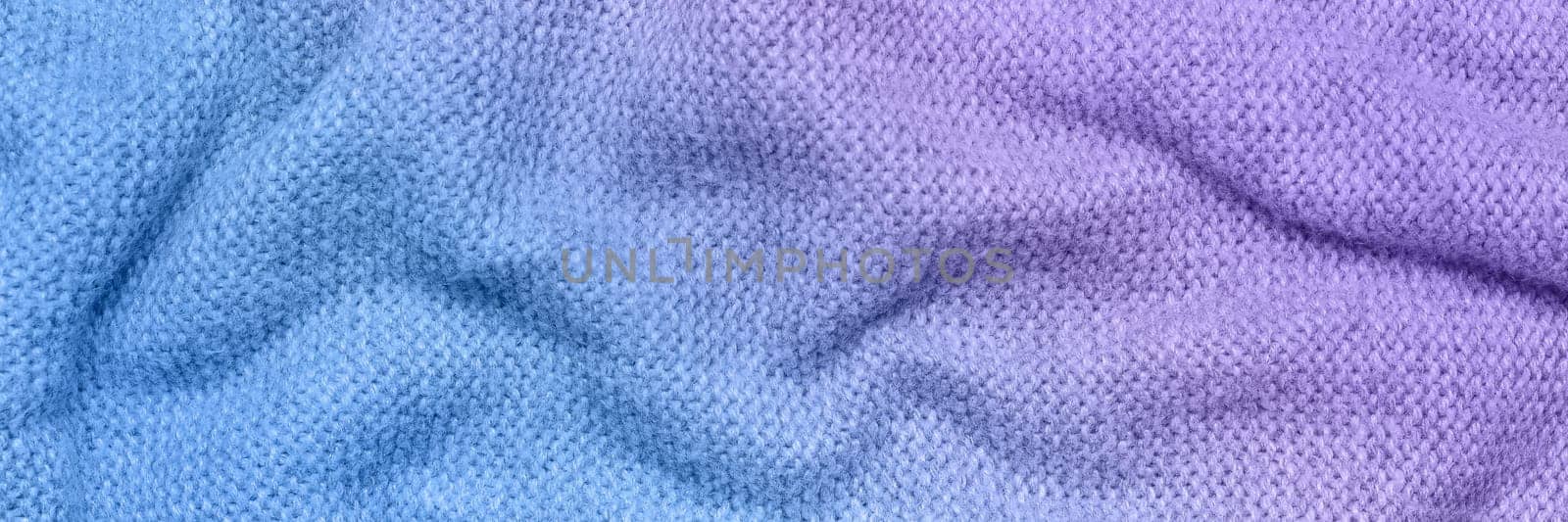 A soft and textured gradient blue and purple knitted fabric with gentle waves and folds, creating a cozy and warm appearance. Ideal for textile backgrounds, fashion, or home decor themes.