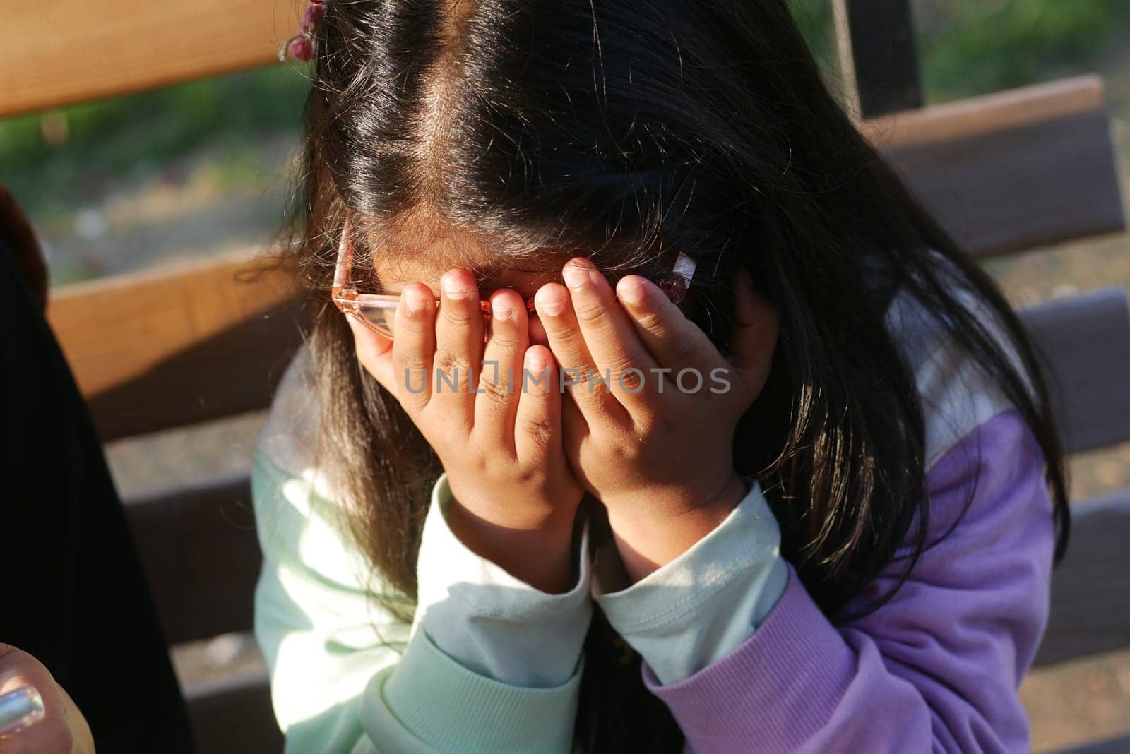 A young girl covers her eyes, hiding from something in the bright sunlight.