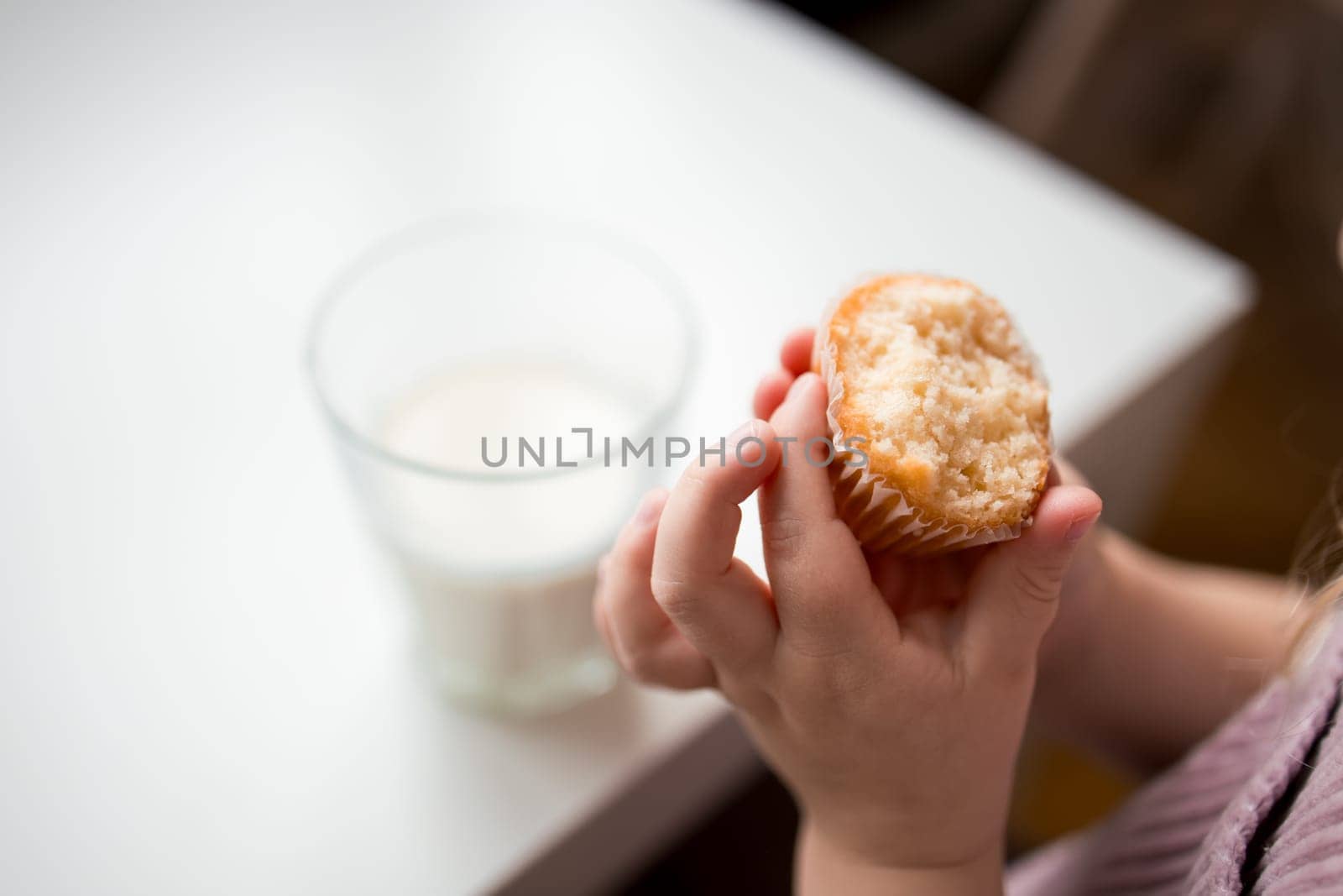 Child enjoying a muffin with a glass of milk at a table.