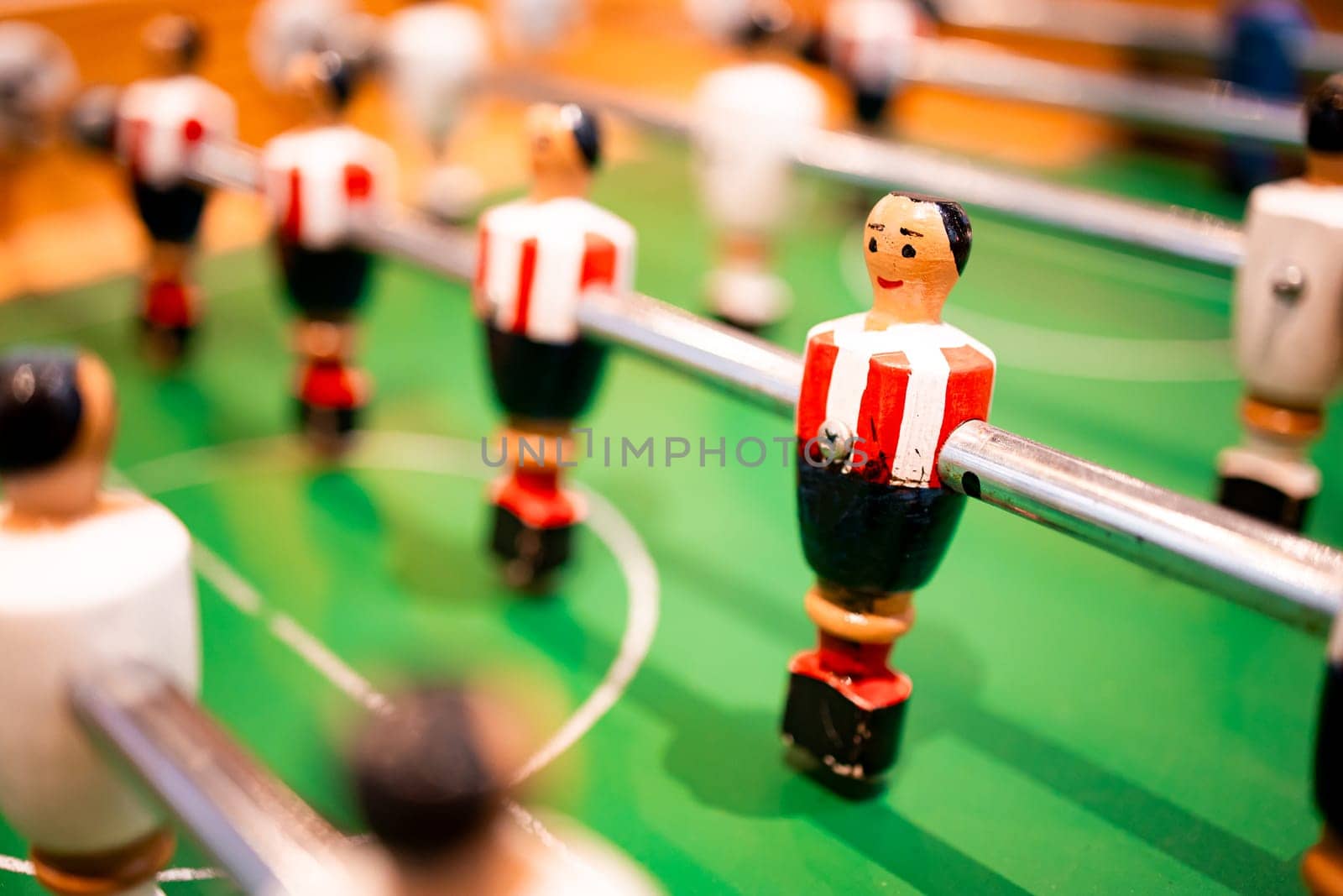 Foosball table close up with red and white figures on green field.