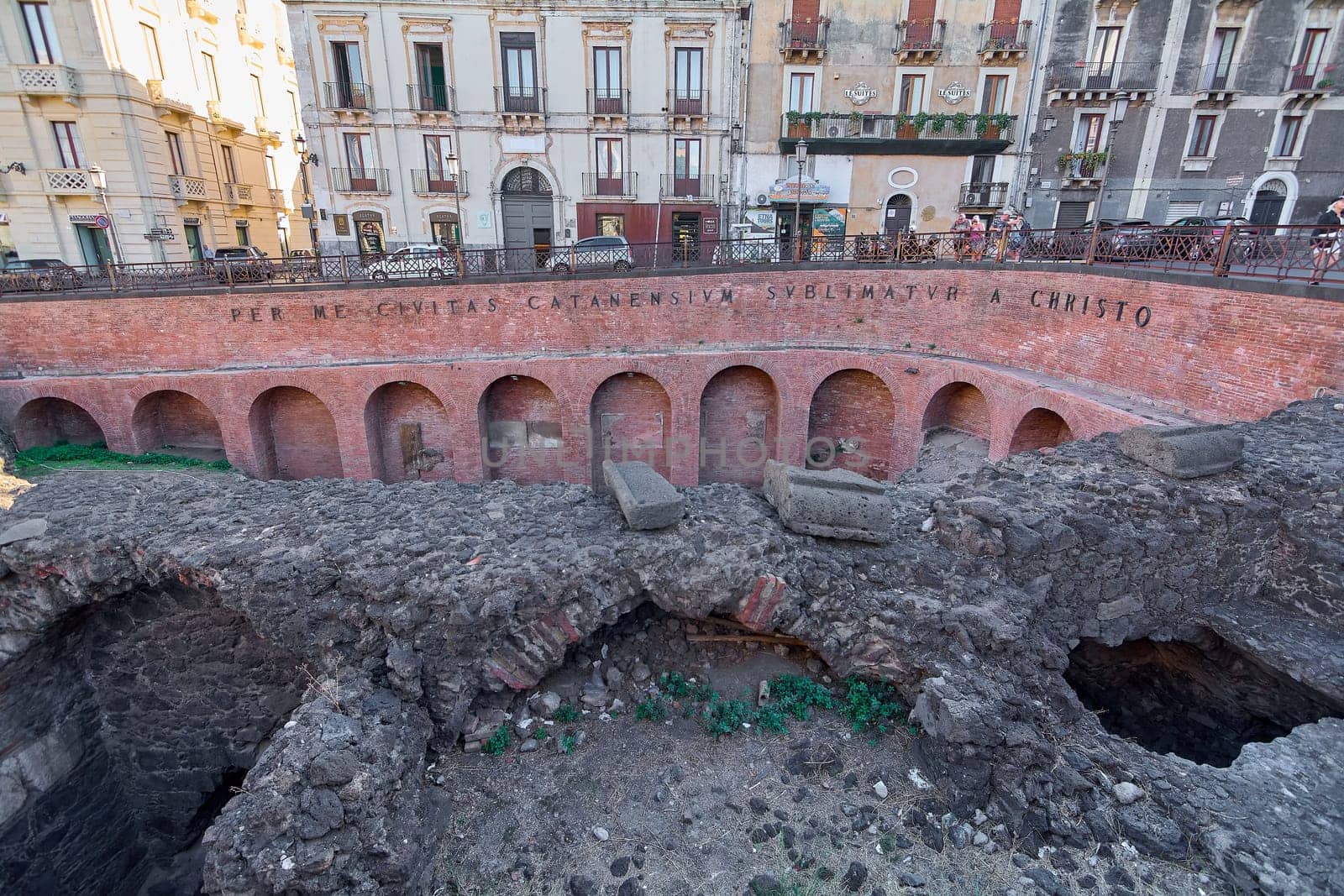 Catania. Italy - March 3, 2025: Stunning Roman Amphitheater excavation with ancient arches and text, set against Catania's vibrant cityscape. Perfect for cultural exploration, historical studies.