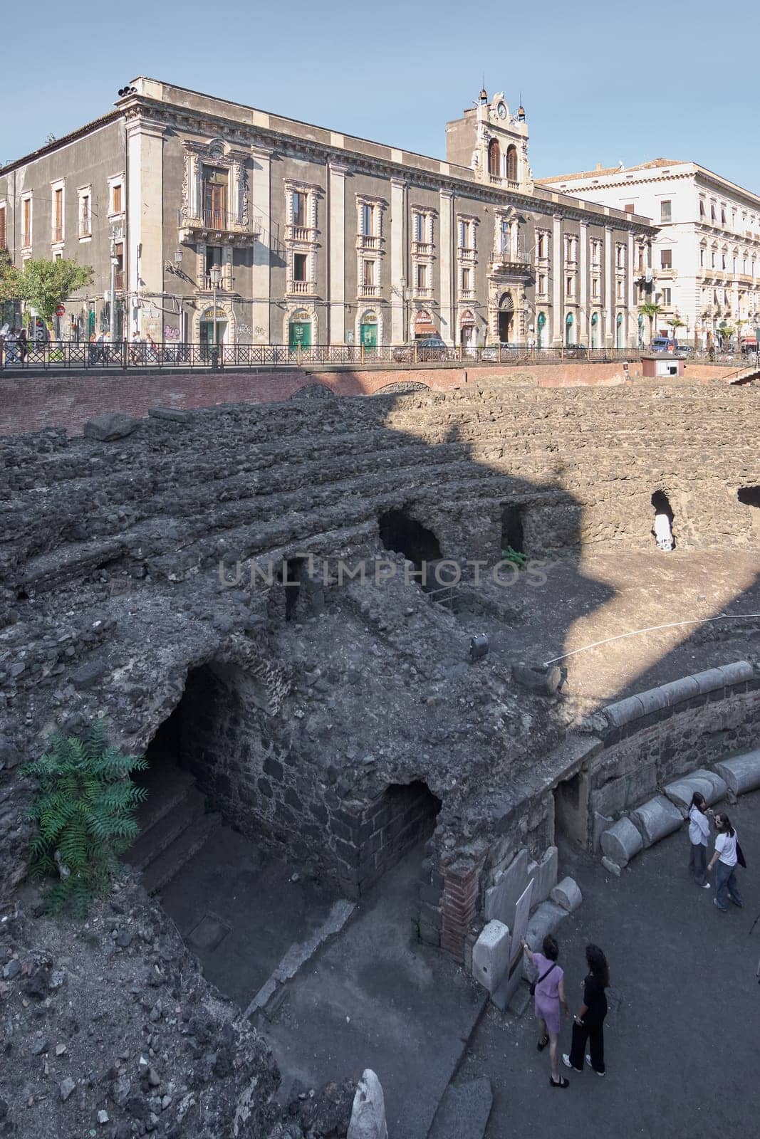 Catania. Italy - March 3, 2025: Ancient Roman Amphitheater ruins with tourists exploring stone arches and columns Captures historical depth and modern interest under a clear sky, ideal for archaeology