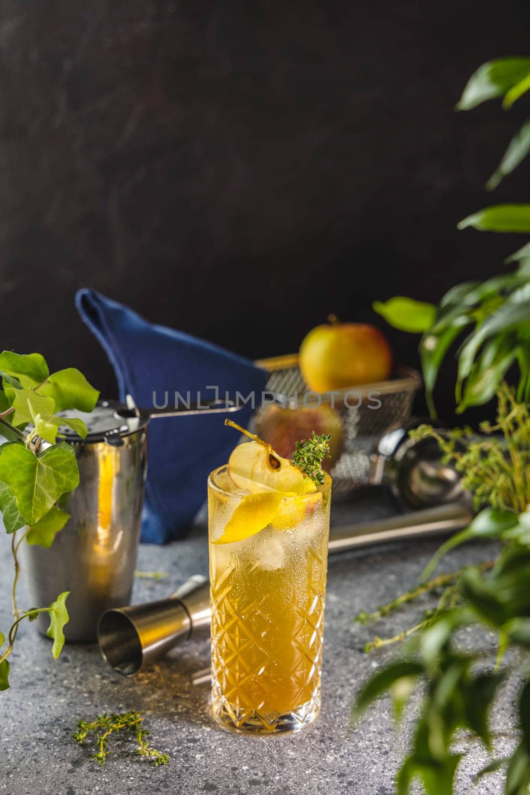 Ice cold apple cocktail garnished with fruit slices and thyme served in a crystal glass on a bar counter