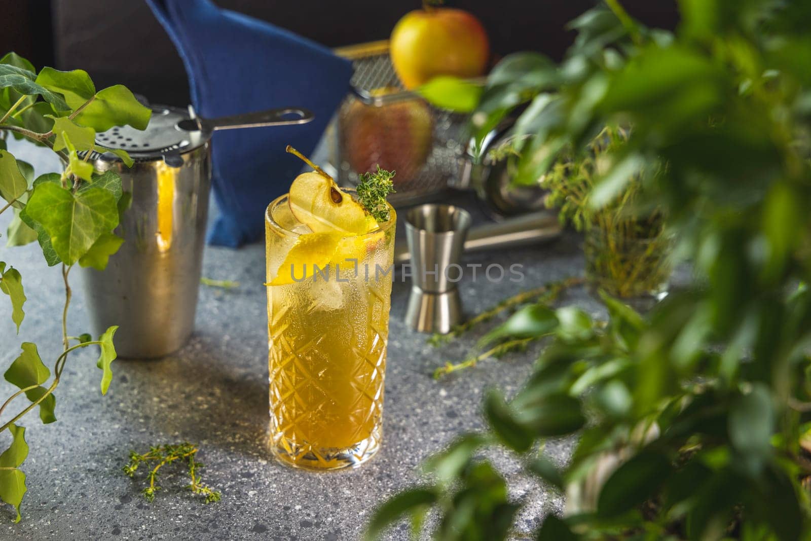 Refreshing apple and pear cocktail being prepared with fresh herbs, shaker, and jigger on a bar counter