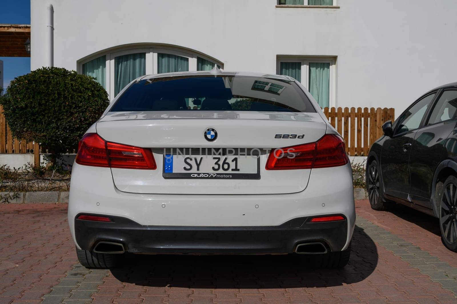 Gaziveren Cyprus -01.03.2025 A sleek white luxury sedan is parked in front of a stylish modern building under clear blue skies.