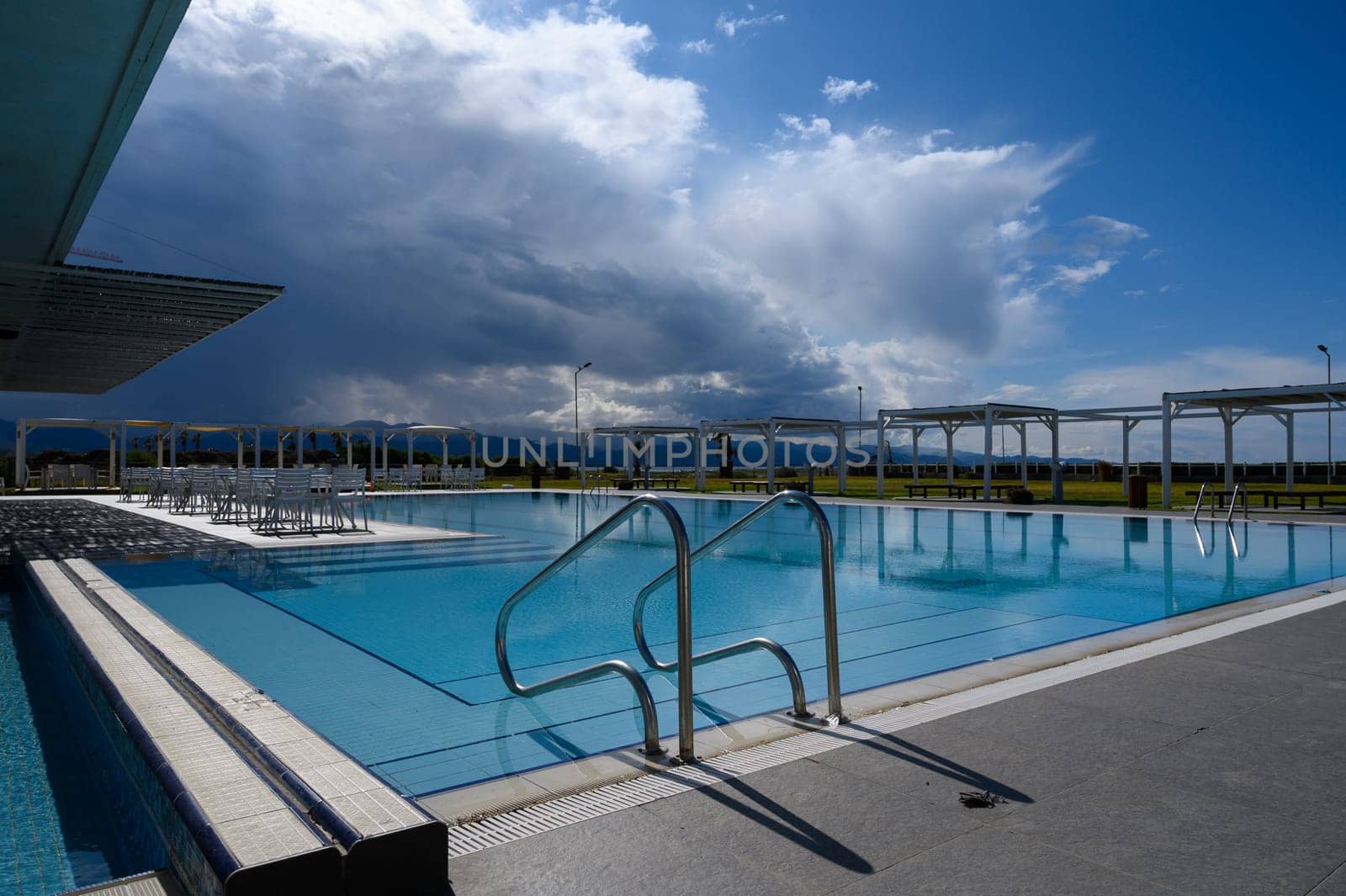 Tranquil poolside escape shines under sunlight as storm clouds loom, inviting relaxation and serenity in the afternoon.