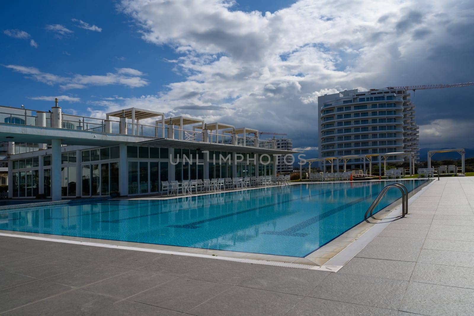 Soothing poolside atmosphere invites relaxation amid a striking backdrop of modern architecture and gentle clouds.