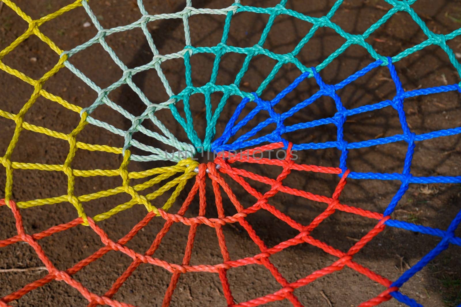 Brightly colored ropes form a spiral web, revealing stunning patterns against a textured ground in daylight.