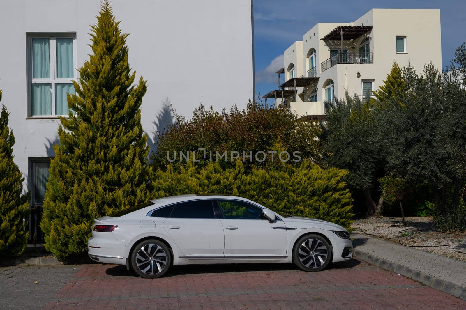 Gaziveren Cyprus -01.03.2025 A sleek white car stands beside vibrant green trees, offering a glimpse of tranquility in a modern residential setting.