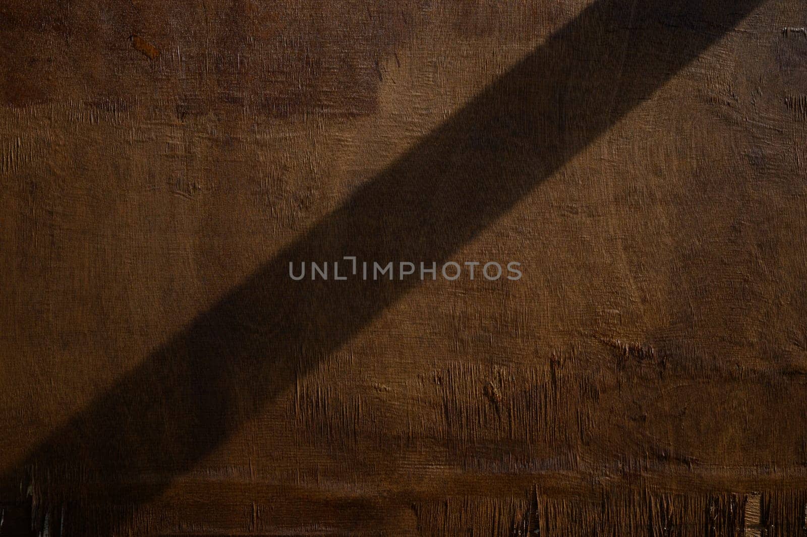 Soft light casts an elongated shadow, creating an artistic interplay on a rustic, textured surface in warm hues.