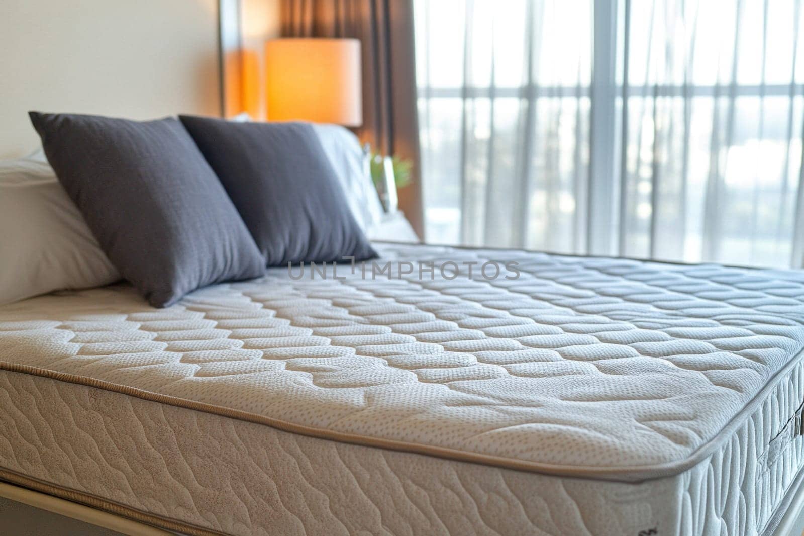 Comfortable mattress and pillows setting on bed with lamp and curtains in bedroom interior design showing hotel room or apartment suite