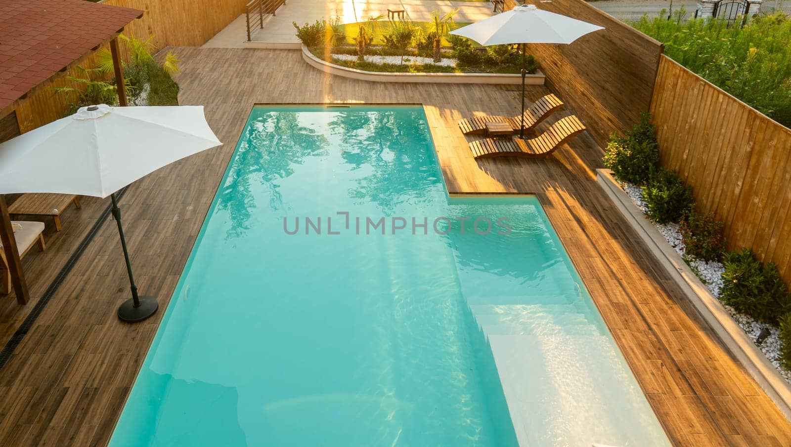 Elegant swimming pool with turquoise water, wooden deck, lounge chairs, umbrellas, and lush greenery in a serene backyard