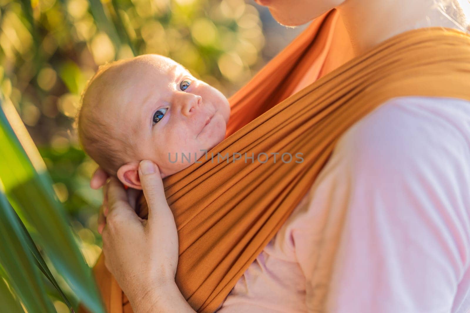 A loving mother walks through a peaceful park, carrying her baby securely in a sling. A heartwarming moment of maternal bonding, babywearing, and the joy of motherhood in nature.