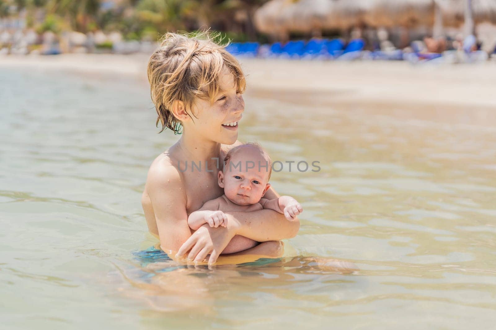 An older brother gently holds his baby sibling while swimming in the sea, sharing a joyful and heartwarming moment of family bonding and summer fun in the water. A perfect blend of love, care, and childhood adventure.