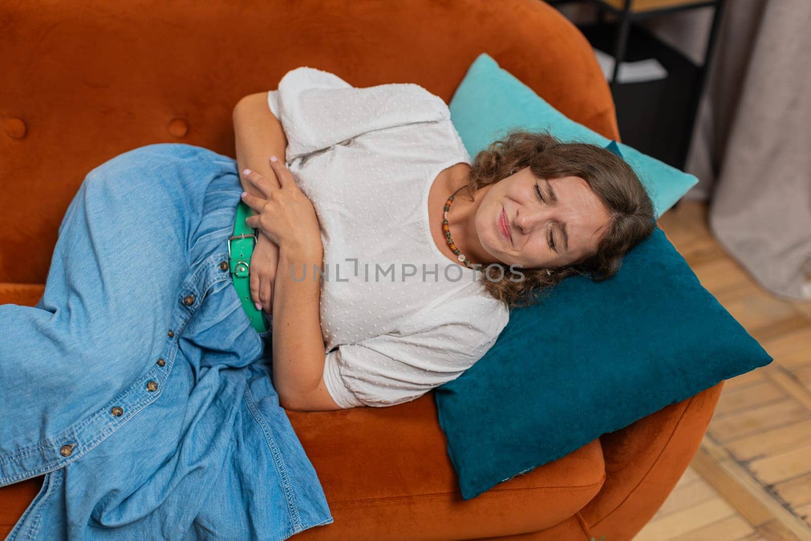 Sick ill woman lady suffering from period cramps, painful stomach ache on sofa at home. Girl holding belly, feeling abdominal menstrual pain. Abdominal pain gastritis diarrhea indigestion. Lifestyles