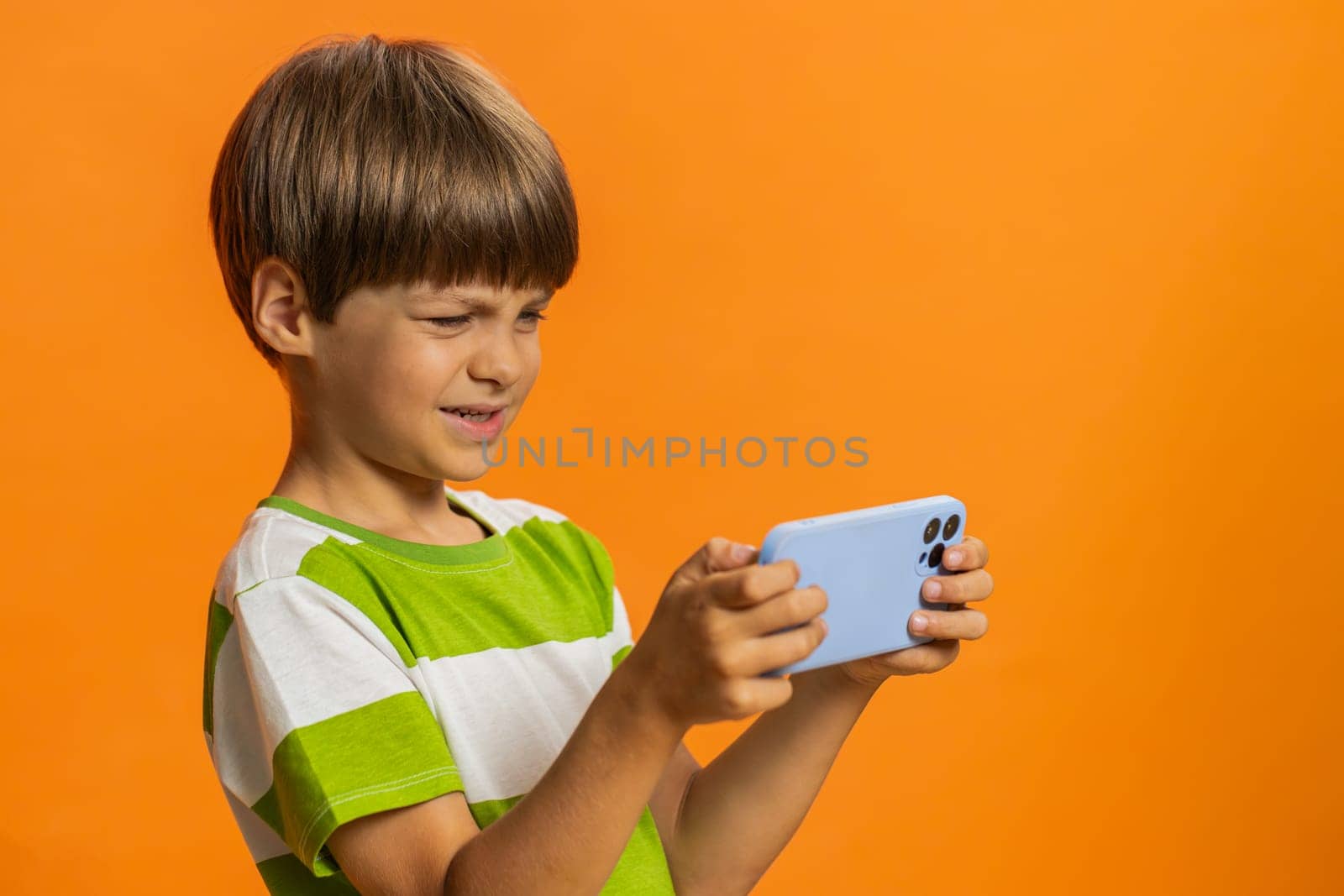 Happy excited young preteen child boy kid player celebrate victory enthusiastically playing racing drive simulator, shooter video games on smartphone. Little children isolated on orange background
