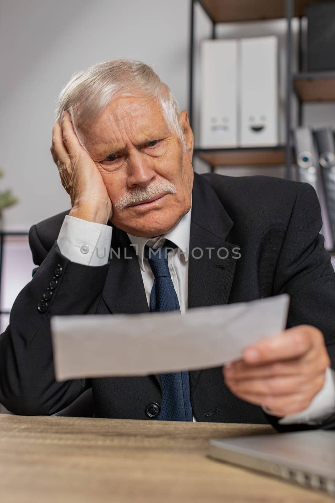 Shocked senior businessman opening envelope reading bad news in letter feels upset. Financial problems, bank debt bill for pay, tax invoice or bankruptcy notification. Guy in suit at home office table