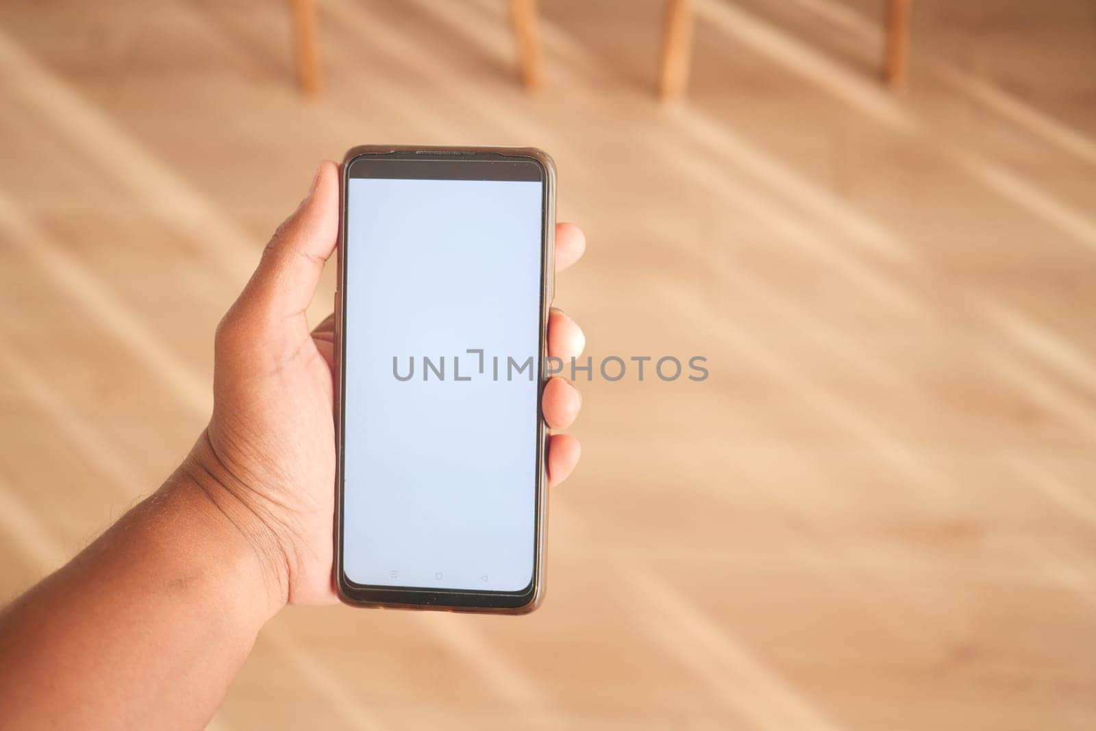 A person holds a smartphone with a blank screen in a bright room.