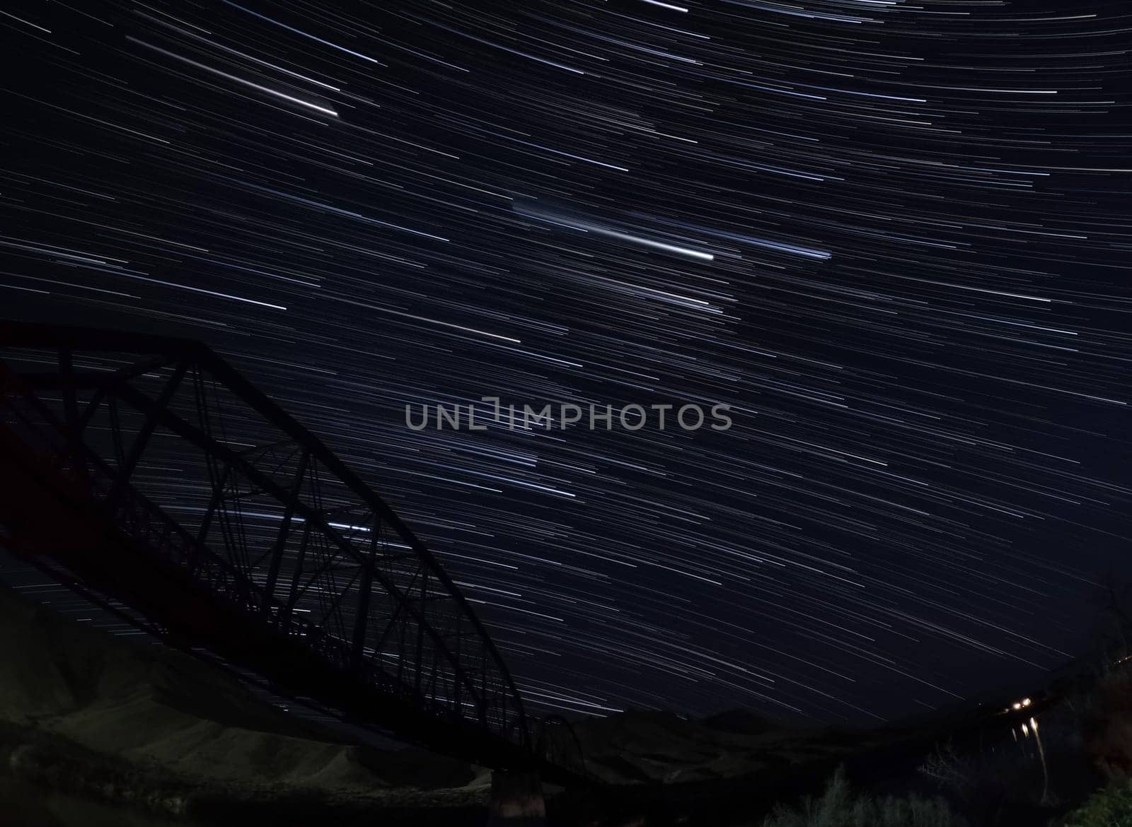The night sky is filled with stars and the bridge is visible in the background. The stars are scattered throughout the sky, creating a sense of wonder and awe. The bridge adds a sense of structure