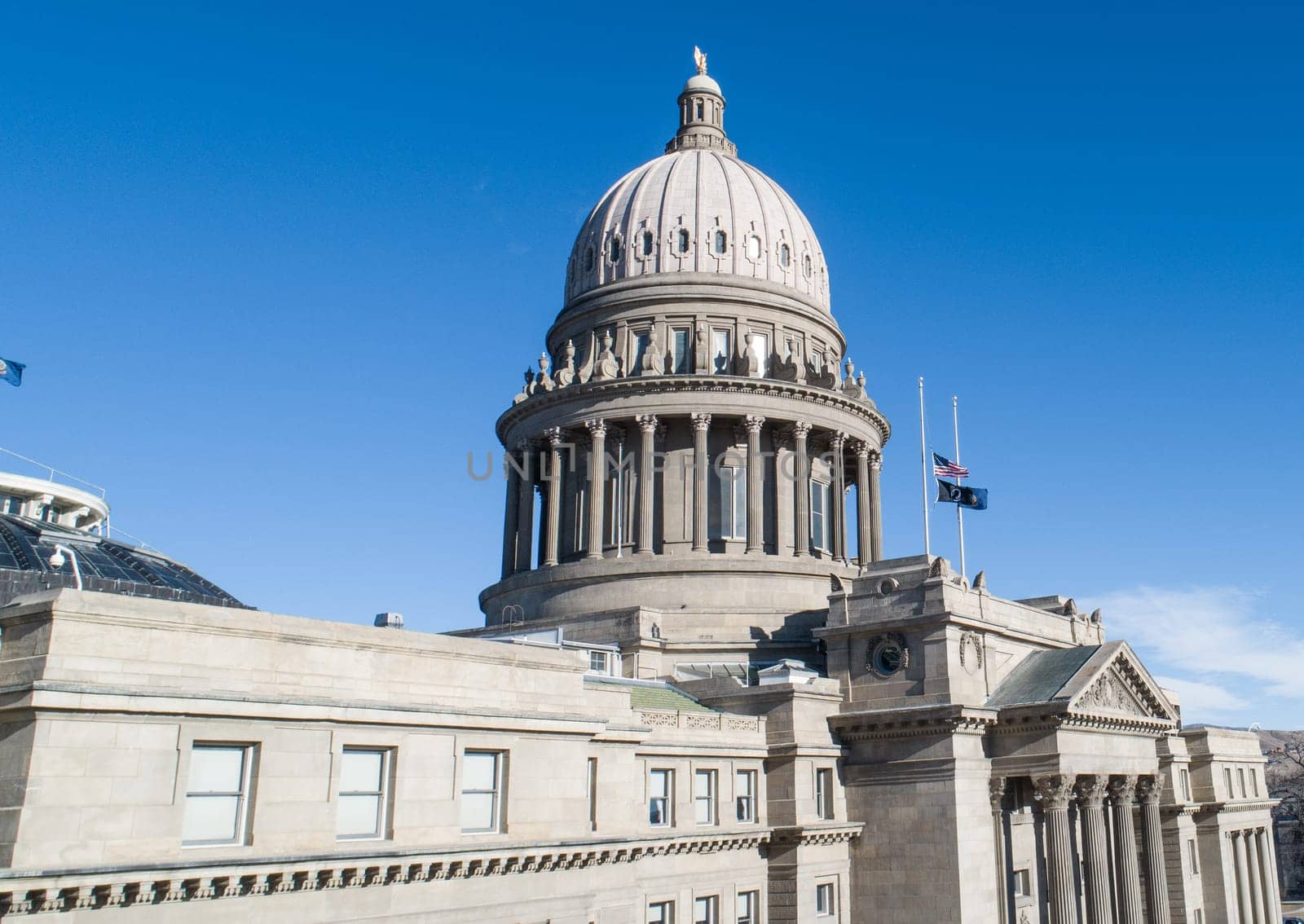 The Boise Capitol building is a large, gray structure with a dome on top. The sky is clear and blue, and there are several flags flying outside the building