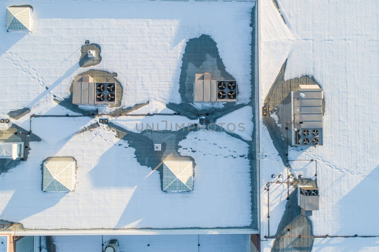 A roof covered in snow, with a few vents and chimneys visible. Scene is calm and peaceful, as the snow covers the roof and the vents and chimneys are barely visible