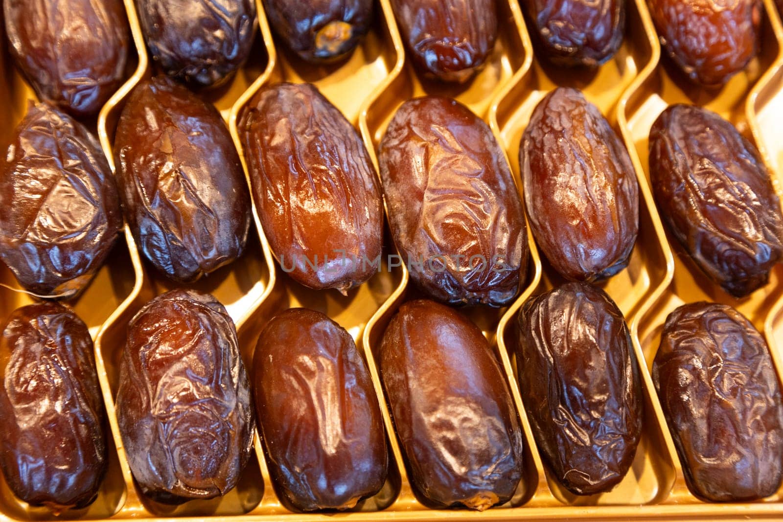 Premium dried dates with a glossy texture arranged in a golden tray. Perfect for food photography, organic produce, healthy eating concepts, and luxurious gift packaging.