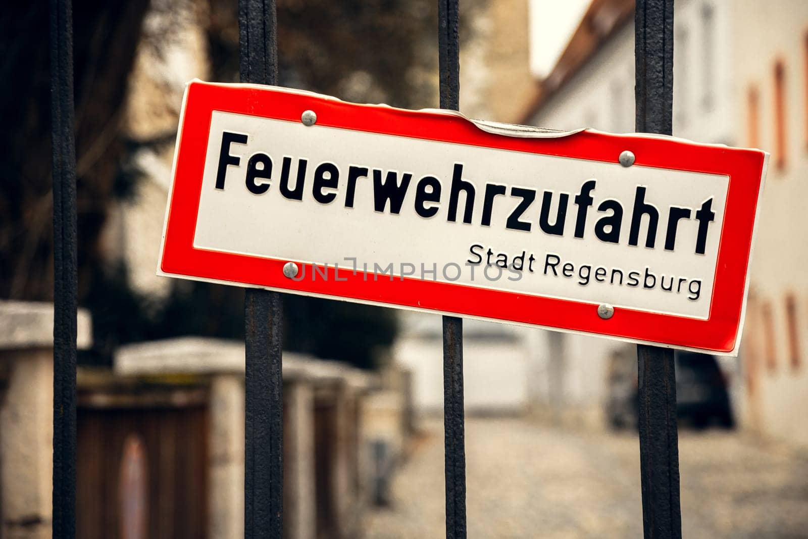 German fire access sign in Regensburg, slightly bent. Close-up of a slightly bent "Feuerwehrzufahrt" sign in Regensburg, Germany. Red and white emergency access sign is mounted on a black metal fence