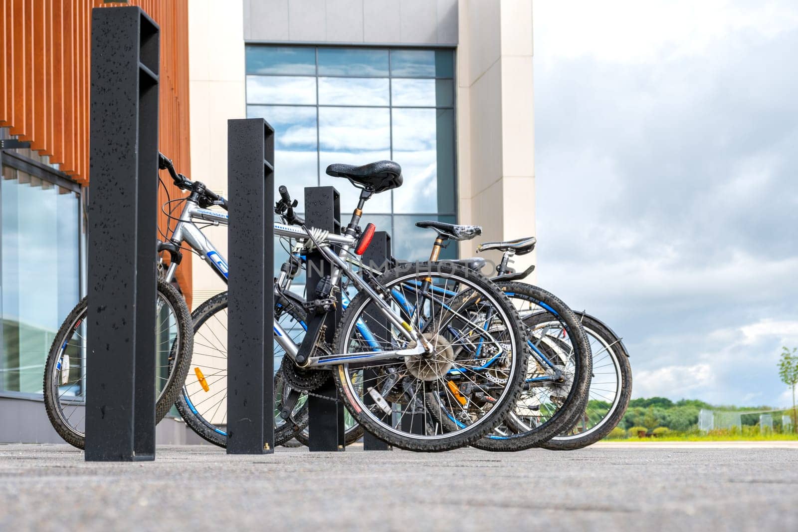 Veliky Novgorod, Russia - 08.01.2024. Bike parking near a modern building in cloudy weather against a backdrop of glass windows and nature.