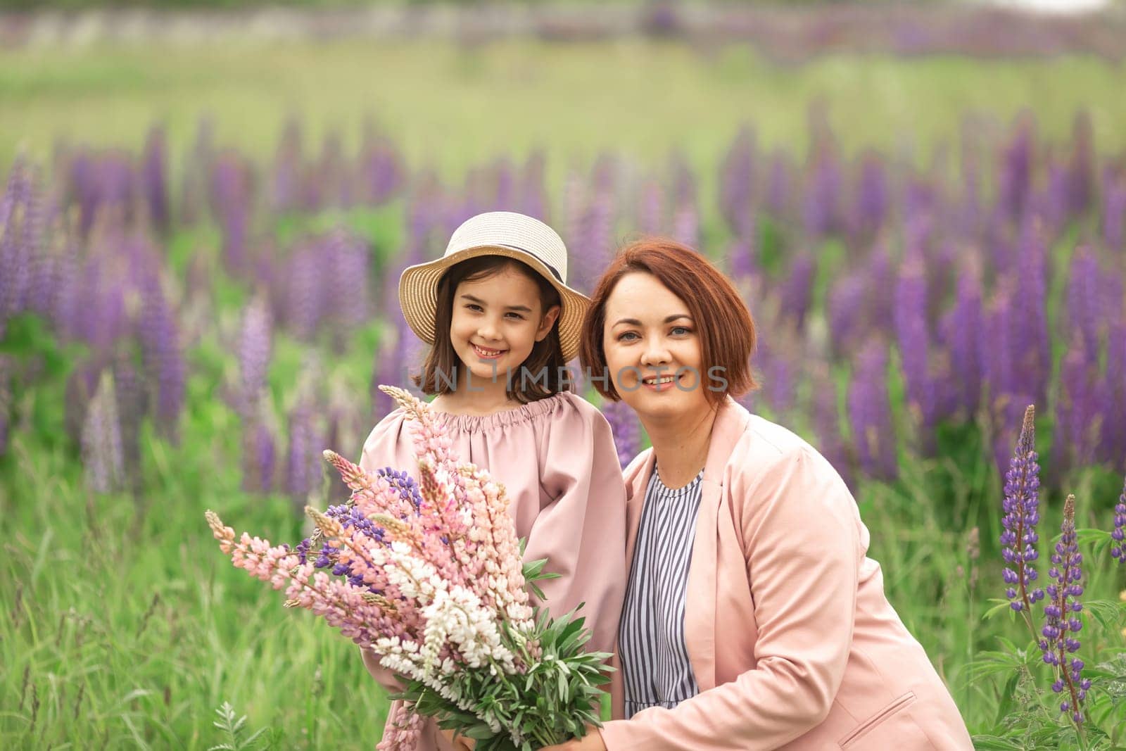 Caucasian woman and young girl smiling in a field of purple lupines on a sunny day.
