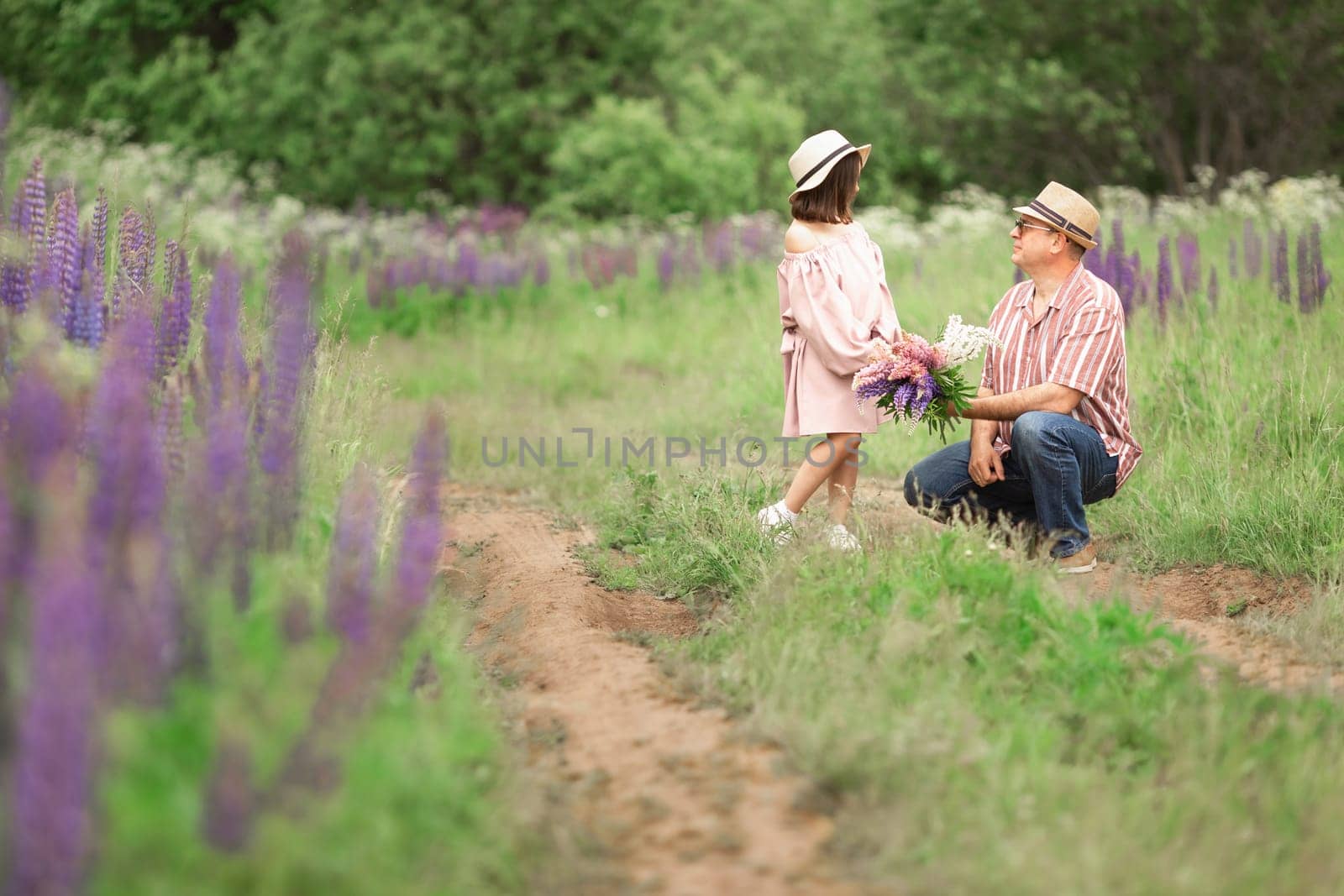 Adult caucasian male and young girl in hat with bouquet in flower field.