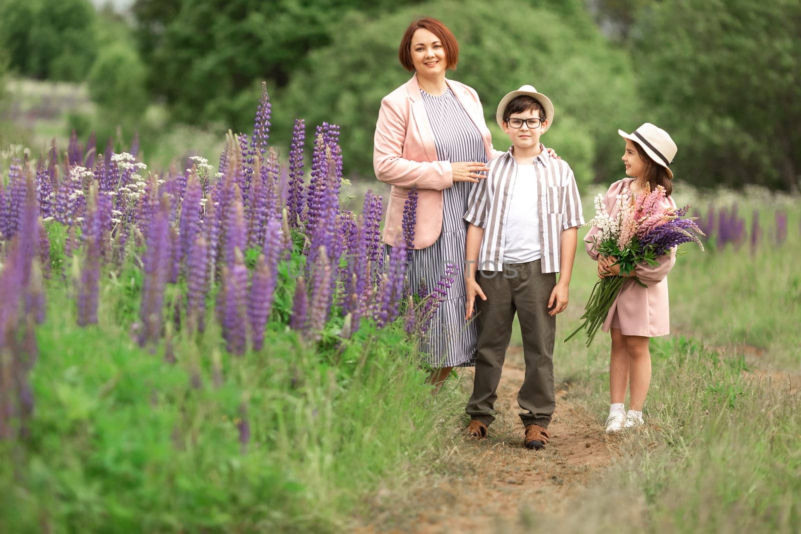 Caucasian mother adult with children in hat and dress walking on nature trail with purple flowers.