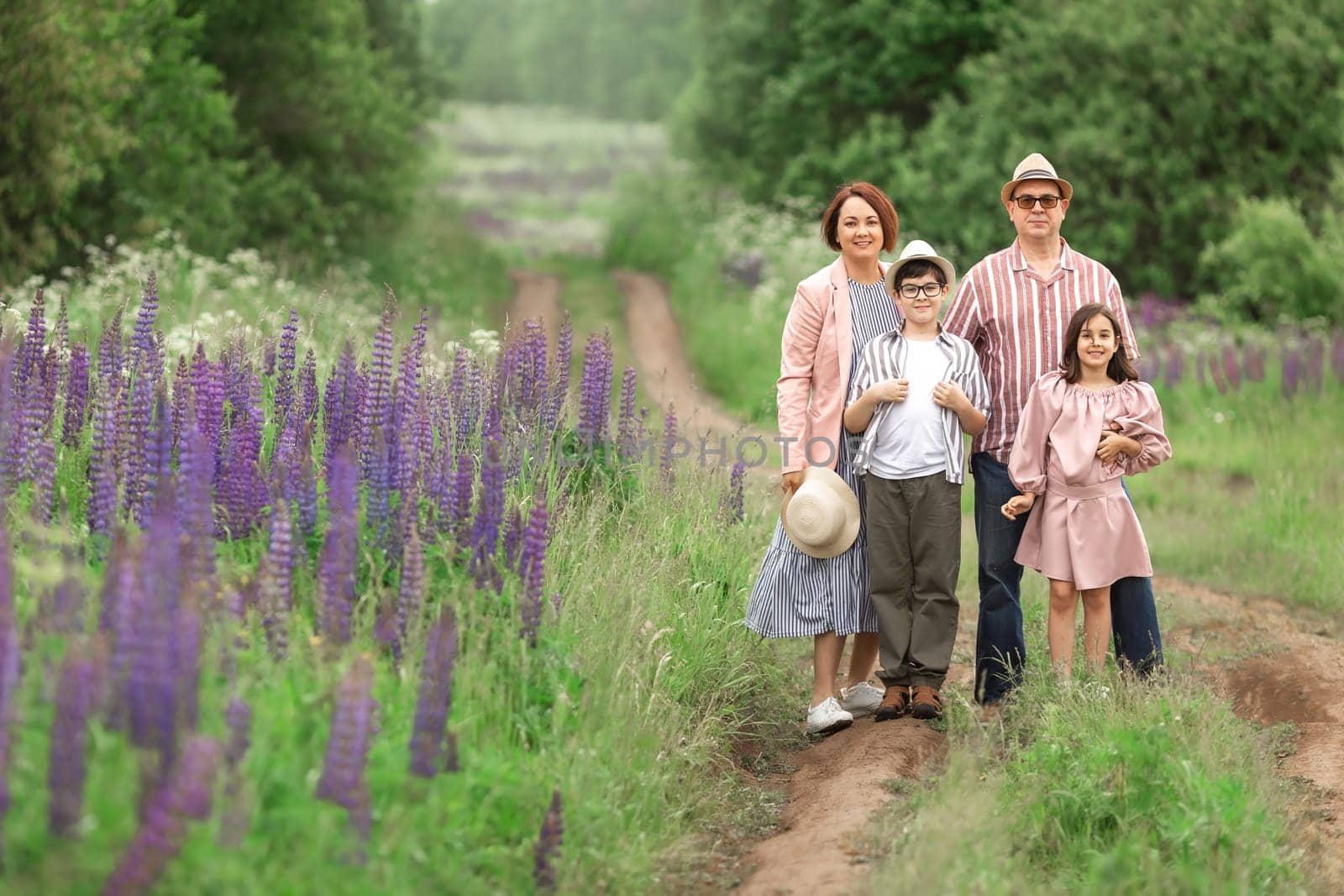Family of four enjoying nature on a path amid purple flowers in a green forest.
