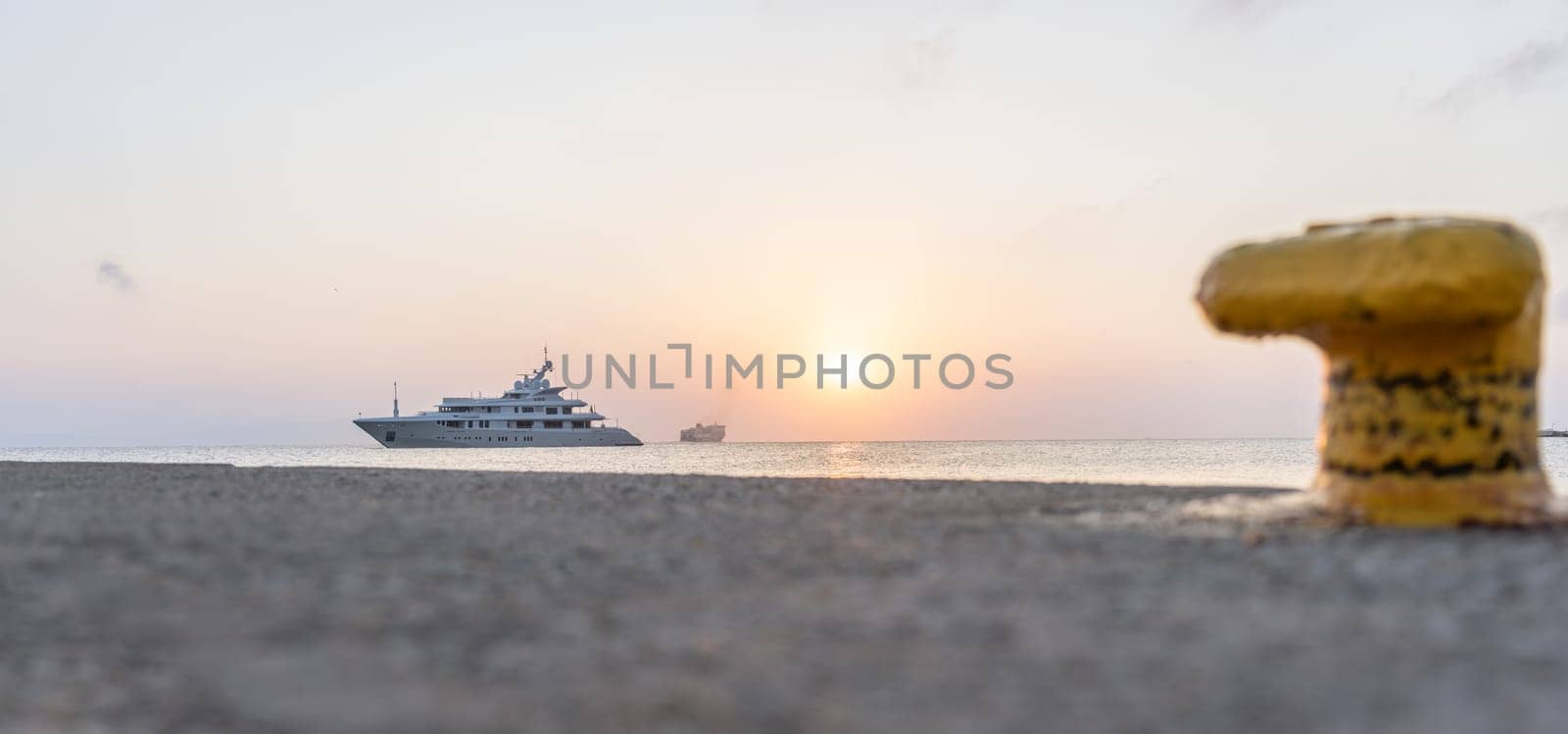 Luxury boat moored off pier on Kos coastline with Blue Star Ferry in background and defocused yellow bollard in foreground