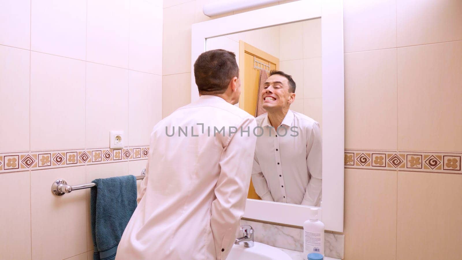 Man in a white shirt checking his teeth in the bathroom mirror after brushing