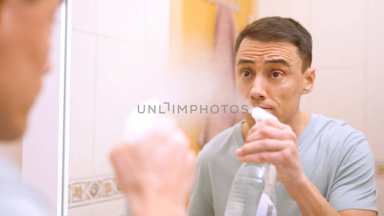 Man spraying cleaning product on bathroom mirror, preparing to wipe and polish