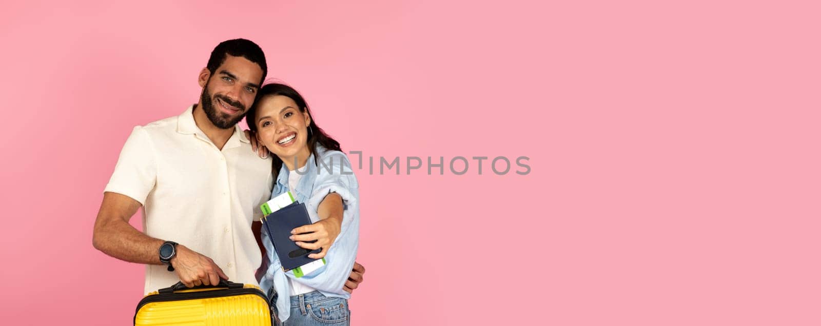 Cute cheerful young hispanic couple travellers going vacation together, carrying luggage, happy man and woman carrying plane tickets and passports, pink background. Summer vacation, trip