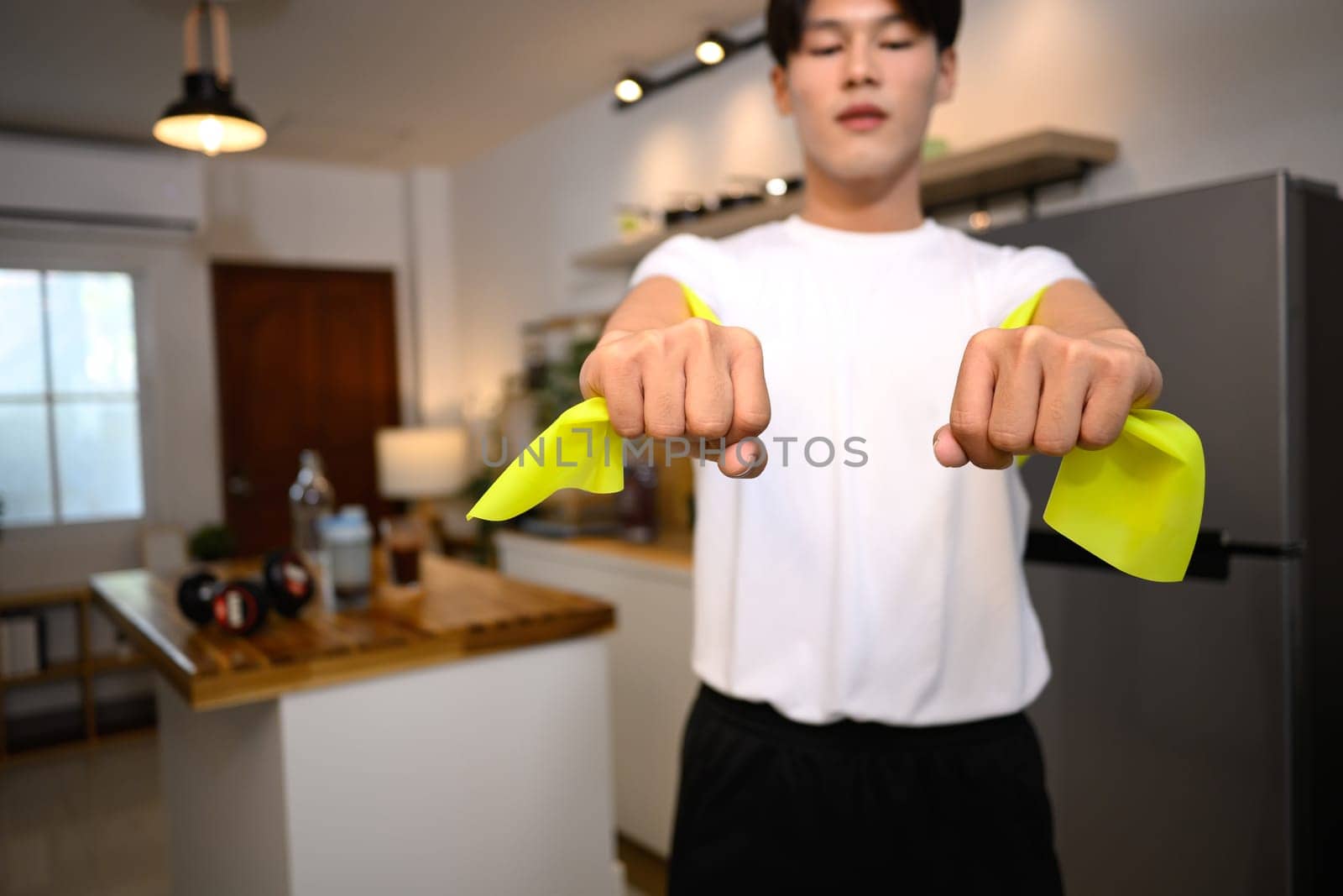 Close up of young man exercising with resistance band in cozy home.