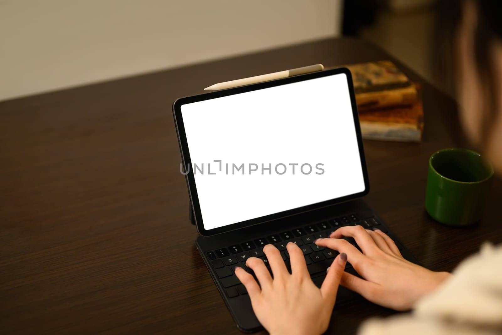 Close up shot of a woman hands typing on digital tablet with keyboard on a wooden dining table.
