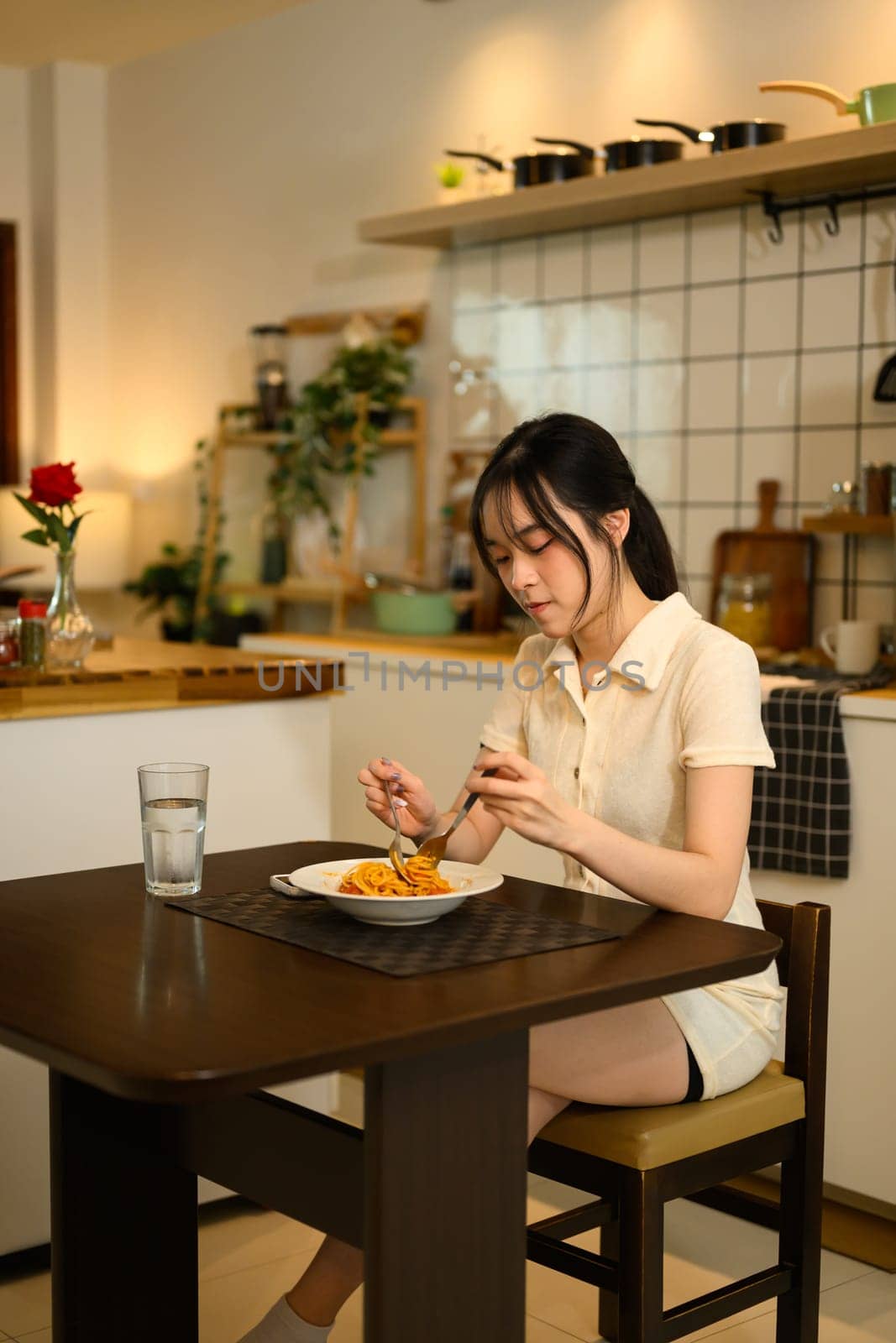 Young woman enjoys a delicious plate of spaghetti in a warm kitchen.