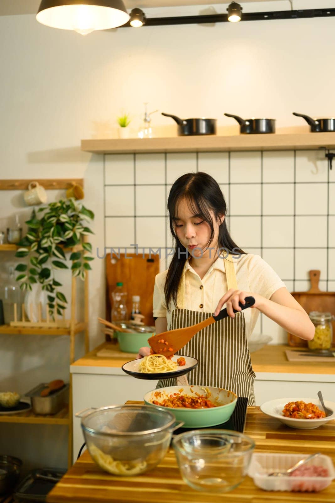 Asian woman stirring rich tomato based sauce on the stove while getting ready to serve freshly prepared pasta dish.