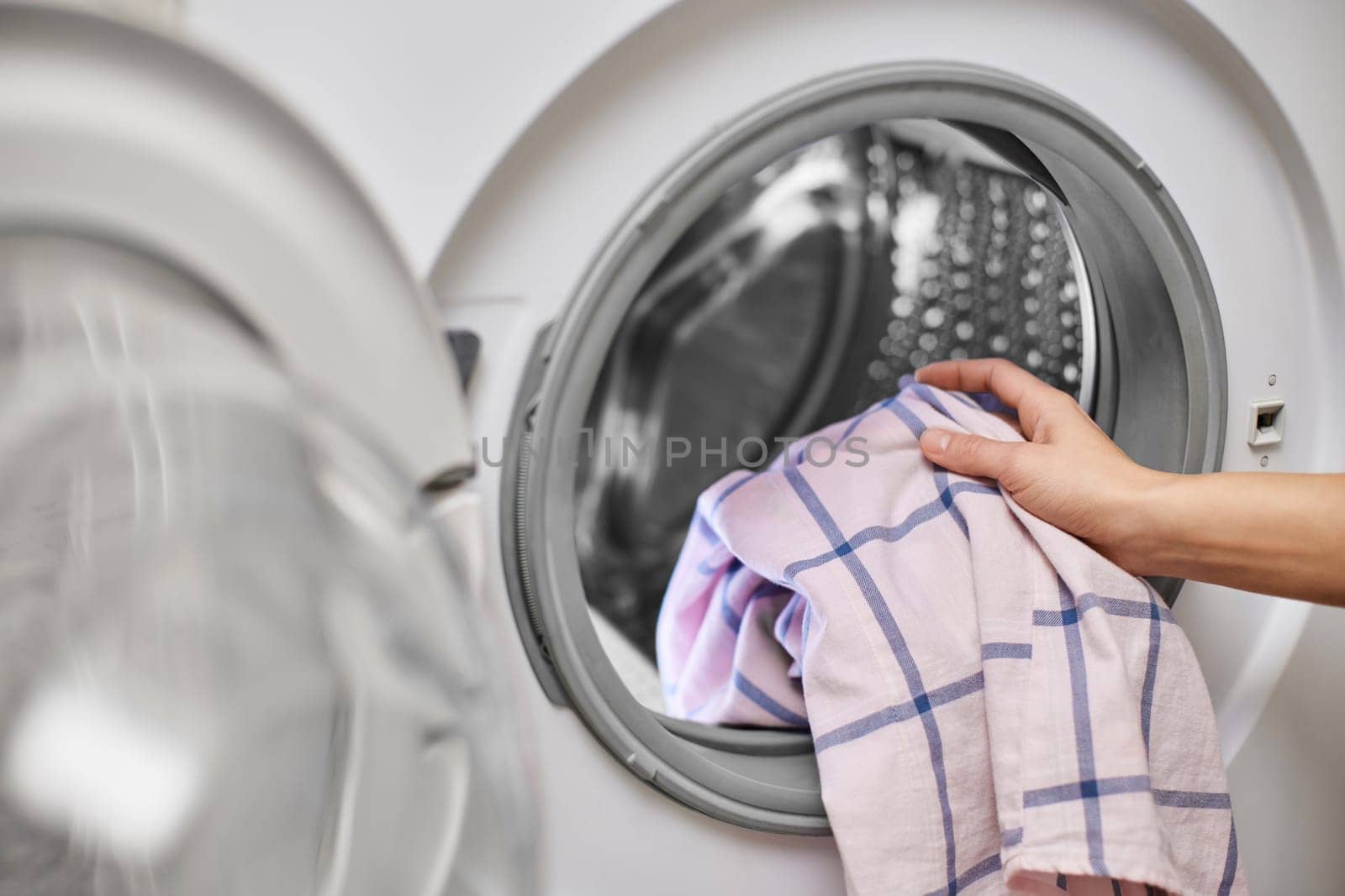 female hand putting color cotton clothes into the washing machine, close-up