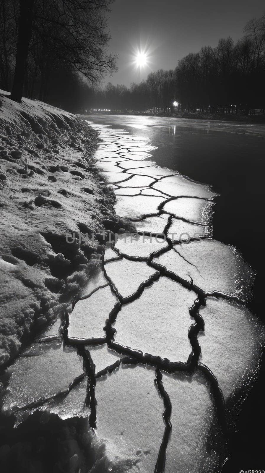 A frozen lake with large cracks running across the ice, each crack creating intricate patterns while the snow-covered shoreline remains still and untouched.