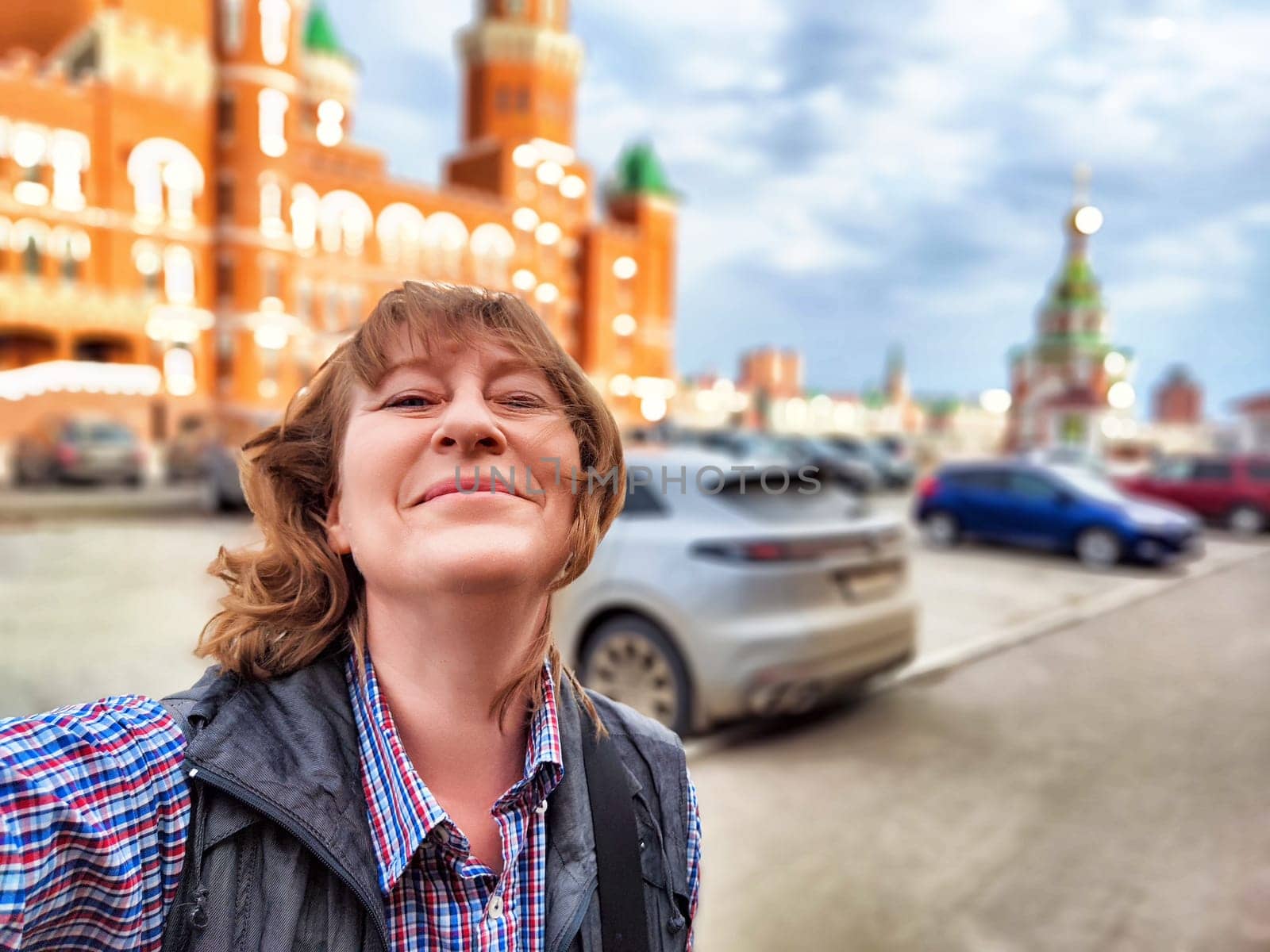 A middle-aged female traveler captures a joyful moment while exploring a lively city on a beautiful day.