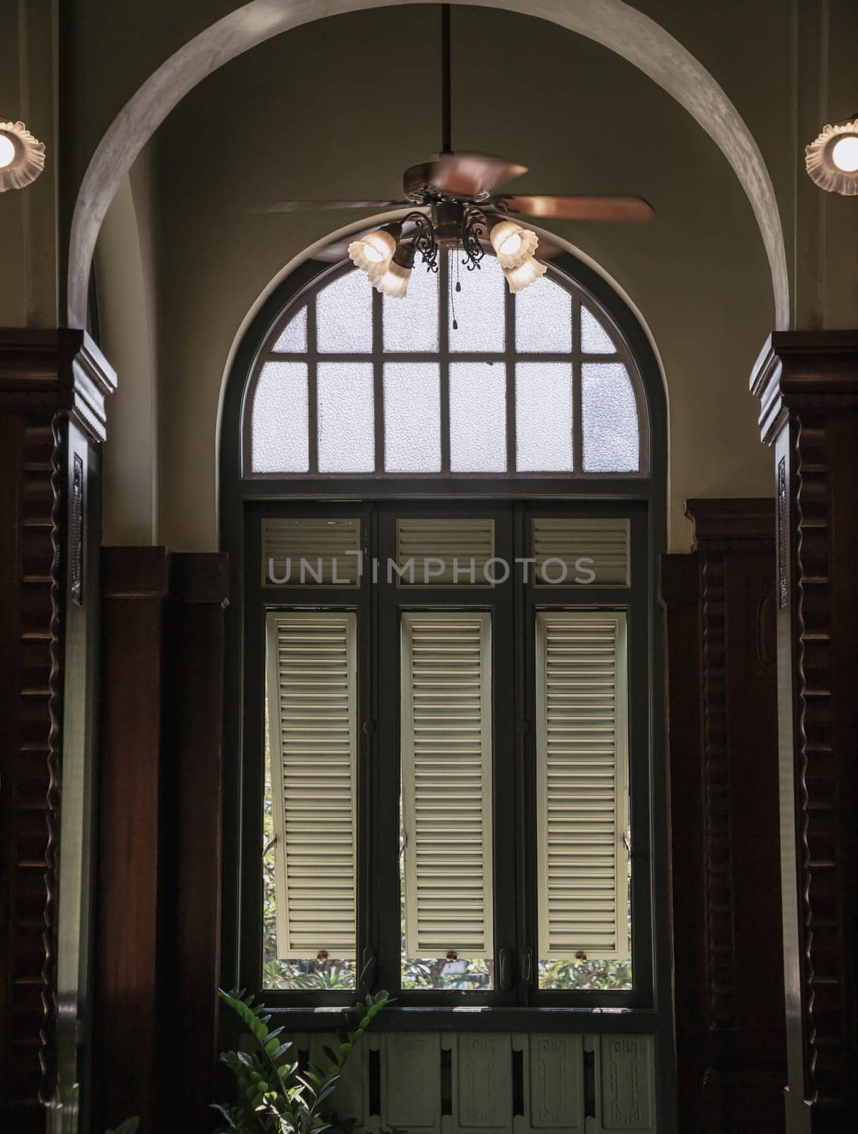 Bangkok, Thailand - Mar 02, 2025 - View of Three wooden louvered window shutters under glass frame inside of Hallway with Vintage ceiling fan and Lamps inside The main Bang Khun Phrom Palace that blends Baroque style with stucco designs. use it as your Wallpaper, Poster and Space for text, Selective focus.